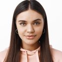 Close up portrait of stylish young modern woman with natural light make up, smiling at camera and look confident, standing against white background.